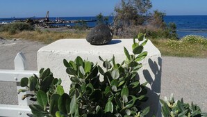 A concrete structure with a rock on top, surrounded by greenery, overlooking a coastal area with a pier and boats.