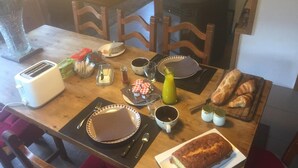 A breakfast table set with bread, croissants, a loaf of bread, a toaster, condiments, and a beverage.