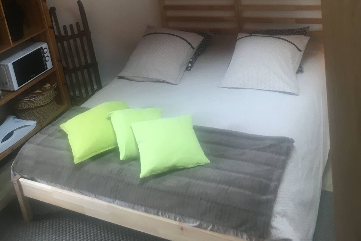 Una habitación pequeña y acogedora con una cama, cabecera de madera, estante con microondas y un cuadro en la pared.