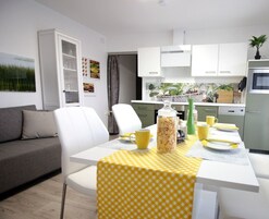 Una cocina moderna con armarios blancos, una mesa de comedor con mantel a cuadros amarillos y una cafetera.