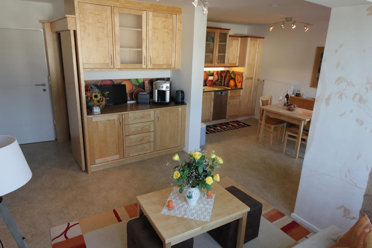 Une cuisine compacte avec des meubles en bois, un coin repas comprenant une table et des chaises, et une petite table agrémentée d’un vase de fleurs.