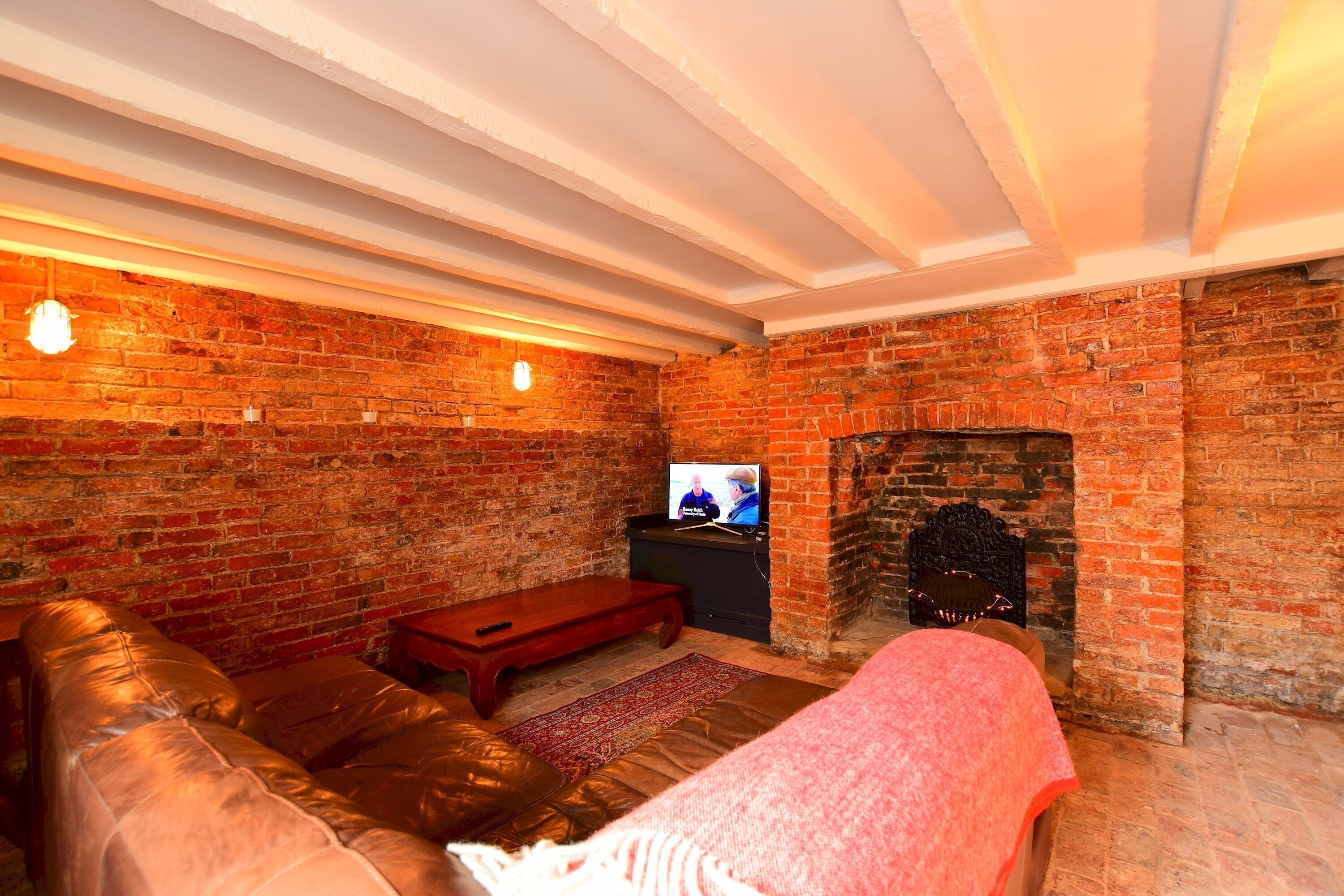Ein gemütliches Wohnzimmer mit Kamin aus Backstein, einem Ledersofa und einem Fernseher.