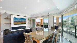 Ein modernes Wohnzimmer mit großem Flachbildfernseher, einem Esstisch mit Glasplatte und einer Couch.