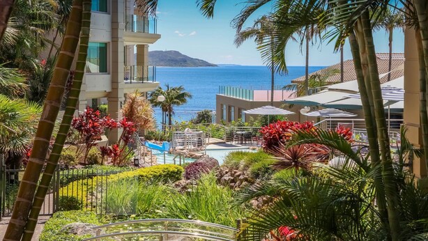 A resort with a pool, palm trees, and a view of the ocean. - Unit 49  - 3 Bed Ocean View (TERRIGAL)