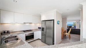 A modern kitchen with white cabinets, a stainless steel refrigerator, a built-in oven, and a granite countertop. - Unit 49  - 3 Bed Ocean View (TERRIGAL)