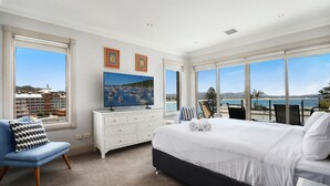 A bedroom with a large bed, a dresser, a TV, and a view of the sea. - Unit 49  - 3 Bed Ocean View (TERRIGAL)