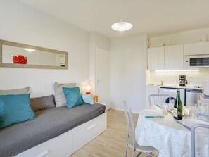 Quarto moderno e bem iluminado, com sofá, mesa de jantar para dois e área de cozinha.