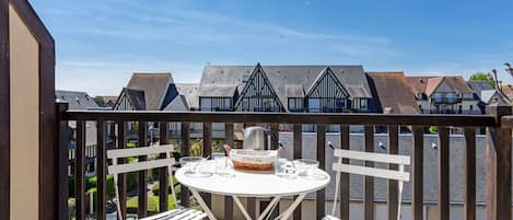 A balcony with a round table and two white chairs, overlooking a row of houses with steeply pitched roofs.