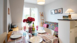 A dining area with a table set for two, a vase of red flowers, and a lamp on a side table. - Lovely apartment for 4 people with WIFI, TV and balcony (Cabourg)