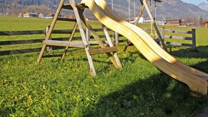 A wooden slide structure in a grassy field with a mountain backdrop.