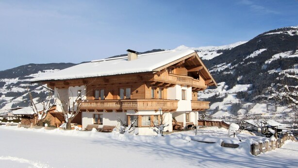 A wooden chalet with a balcony, surrounded by snow-covered mountains.