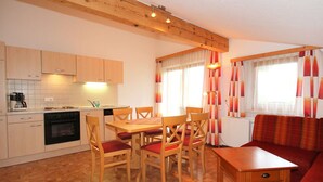 A compact kitchen with wooden cabinets, a stove, and a dining area with a table and chairs.