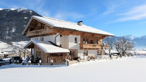 A two-story wooden chalet with a balcony, surrounded by snow-covered mountains.