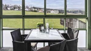 Ein Essbereich mit Tisch und Stühlen, große Fenster mit Blick auf eine Wohngegend.