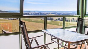 Ein Zimmer mit großem Fenster und Blick auf eine ländliche Landschaft, einem Metalltisch und einem Stuhl.
