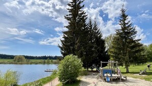 Ein Park am Seeufer mit Spielgeräten, einem Sandbereich und einem Weg zum Wasser.