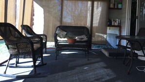 Ein überdachter Patio-Bereich mit Korbmöbeln, darunter zwei Schaukelstühle und ein Sofa mit einer Topfpflanze.