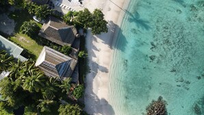 Eine Vogelperspektive zeigt einen Strandort mit Swimmingpool, strohgedeckten Gebäuden und klarem, türkisblauem Wasser.