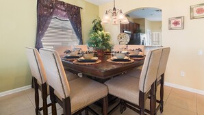 A dining area with a wooden table set for four, surrounded by upholstered chairs. - Pineapple Palms by VillaDirect (Kissimmee)