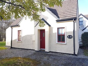 Une maison de plain-pied avec une porte rouge, deux fenêtres aux encadrements rouges et le numéro « 68 » peint sur le mur.