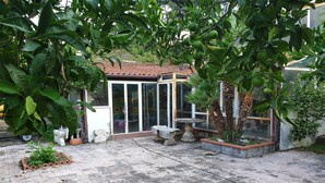 Un patio couvert doté d’un sol carrelé, d’une porte vitrée donnant sur une pièce et de divers pots de plantes.