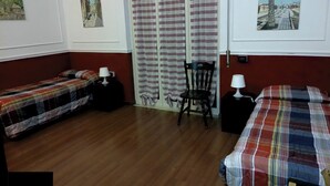 Une chambre avec deux lits, une chaise, une table et une porte avec des rideaux à rayures.