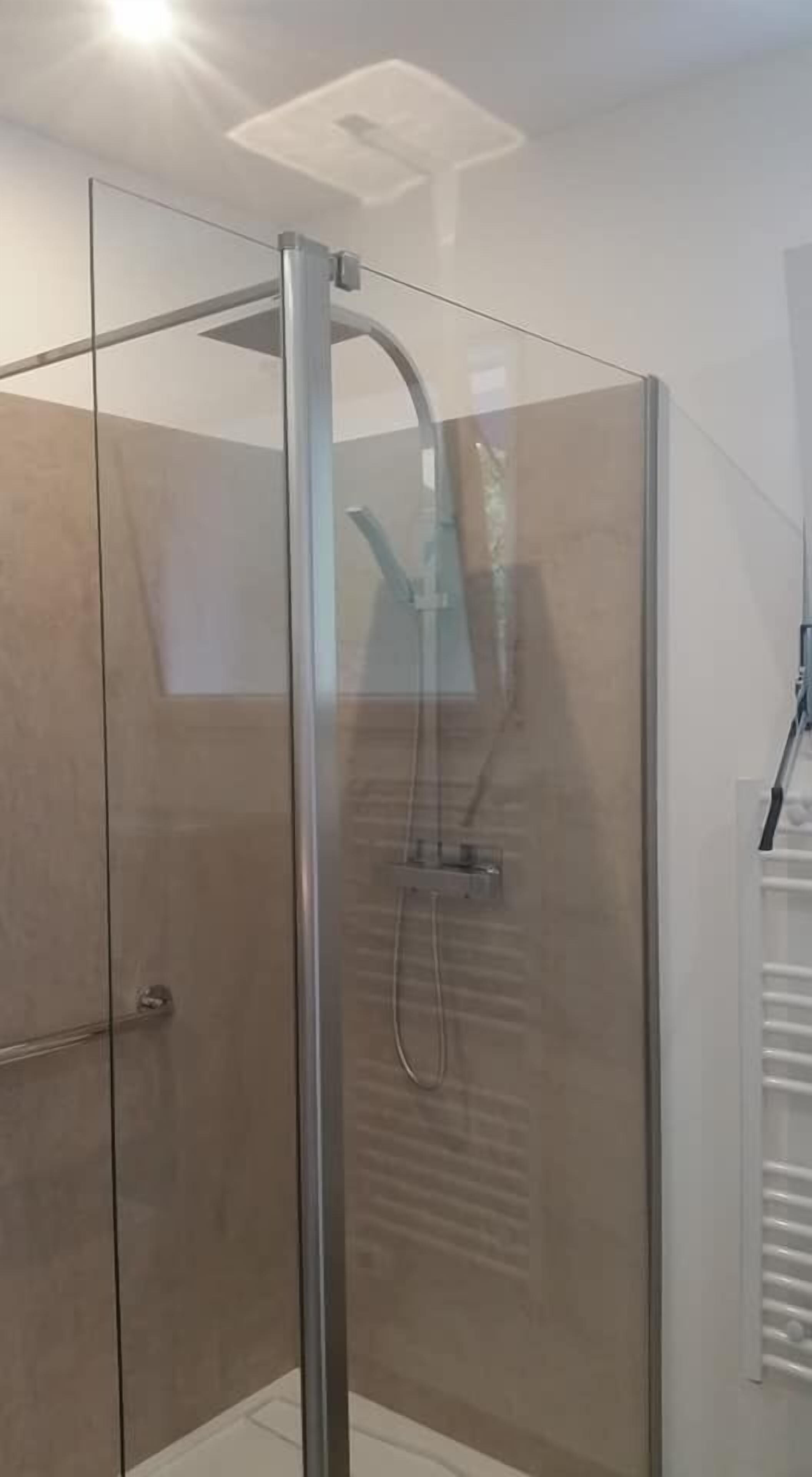 A glass-enclosed shower with a handheld showerhead and a wall-mounted faucet.