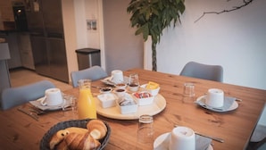 A breakfast setting with a wooden table, various breakfast items, and a plant in the background. - Les chambres de Toucas (Sollies-Toucas)