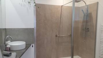 Ein modernes Badezimmer mit einer gläsernen Duschkabine, einem weißen Waschbecken und einem Handtuch.