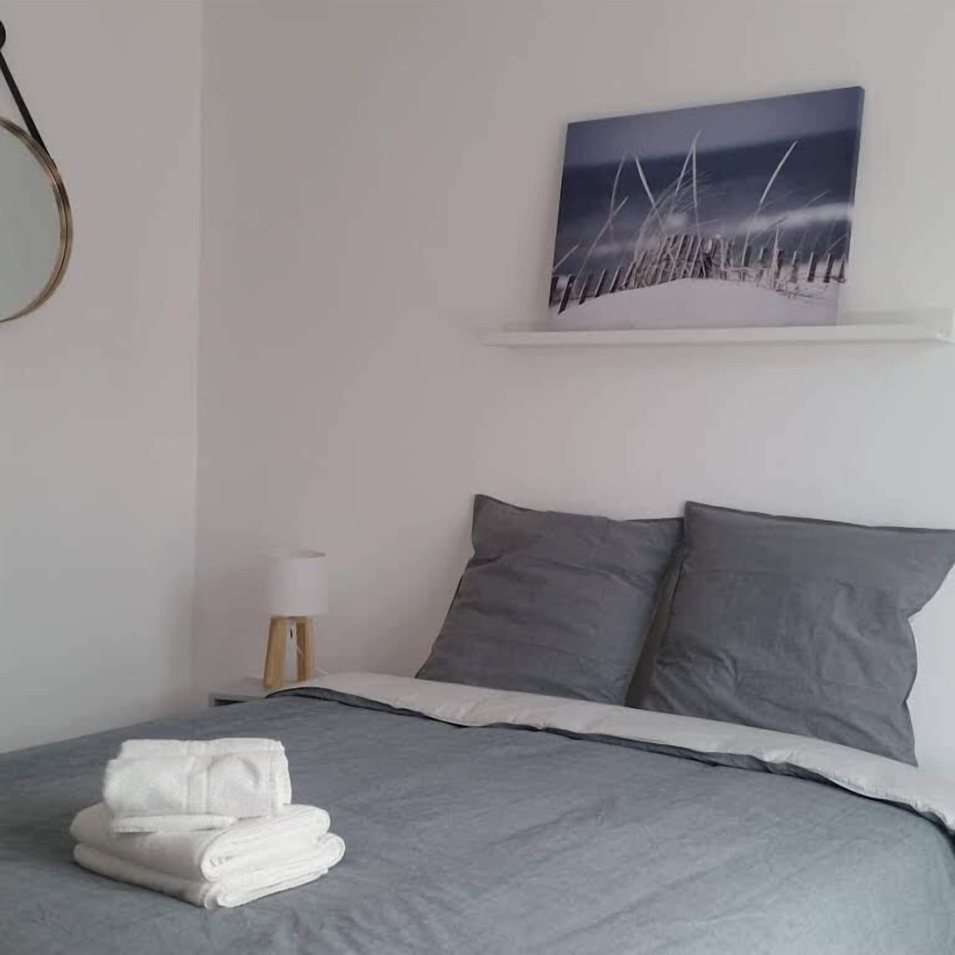 A bedroom with a bed, pillows, a lamp, and a painting on the wall.