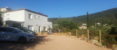 A white building with a tiled roof, a gravel driveway, and a stone wall.