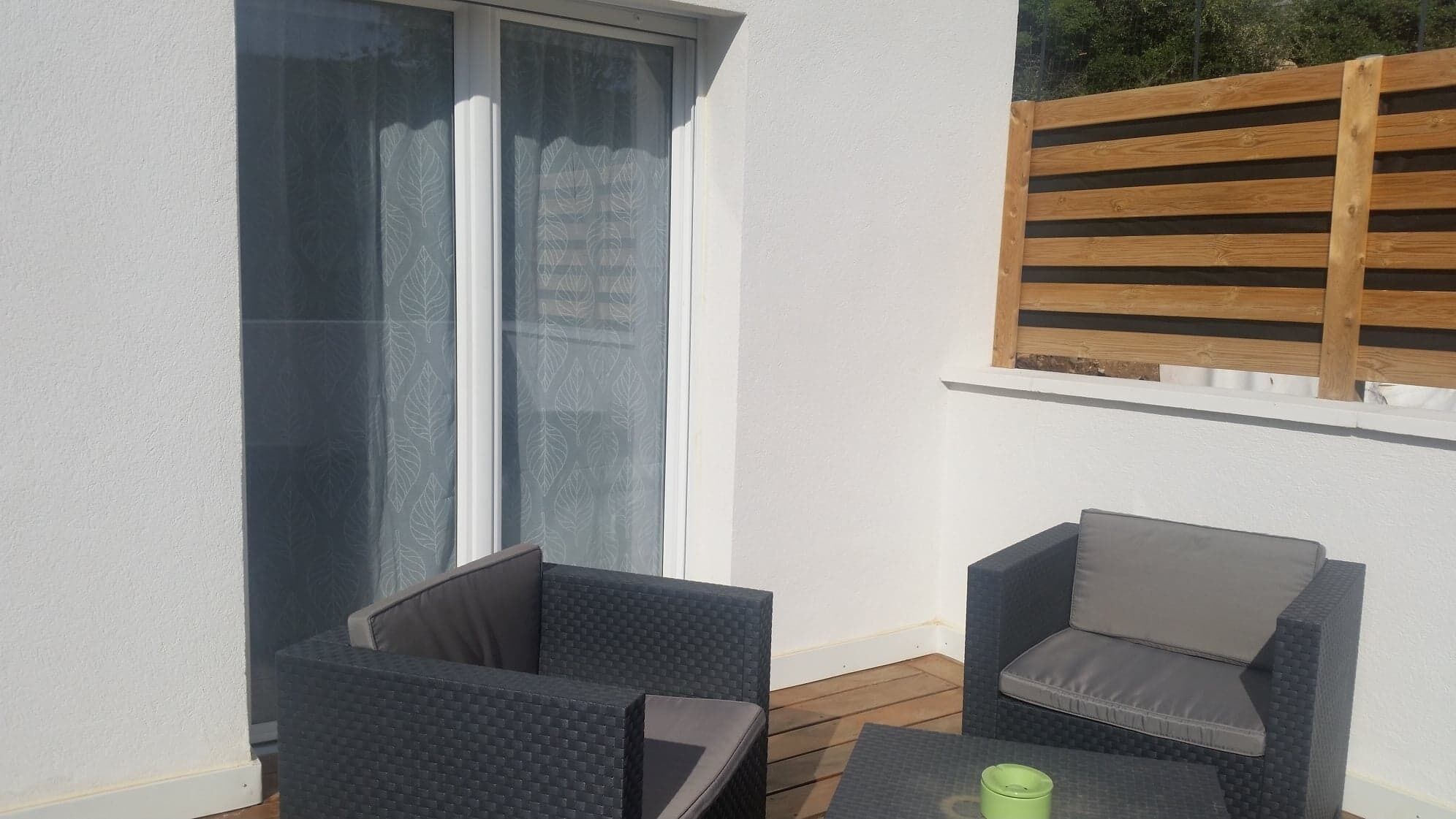 A balcony with two dark wicker chairs, a small table, and a wooden trellis.