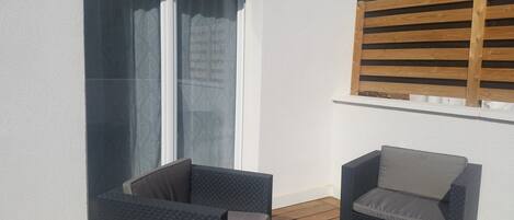 A balcony with two dark wicker chairs, a small table, and a wooden trellis.
