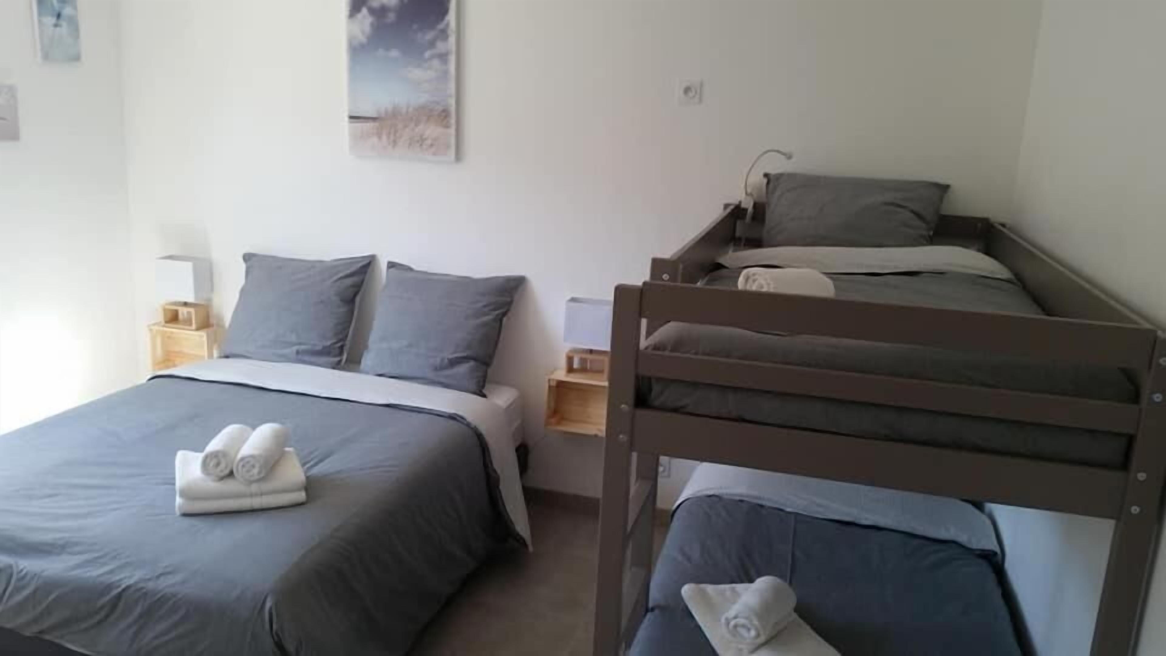 A bedroom with a single bed, a bunk bed, a bedside table, a lamp, and a wall-mounted picture.