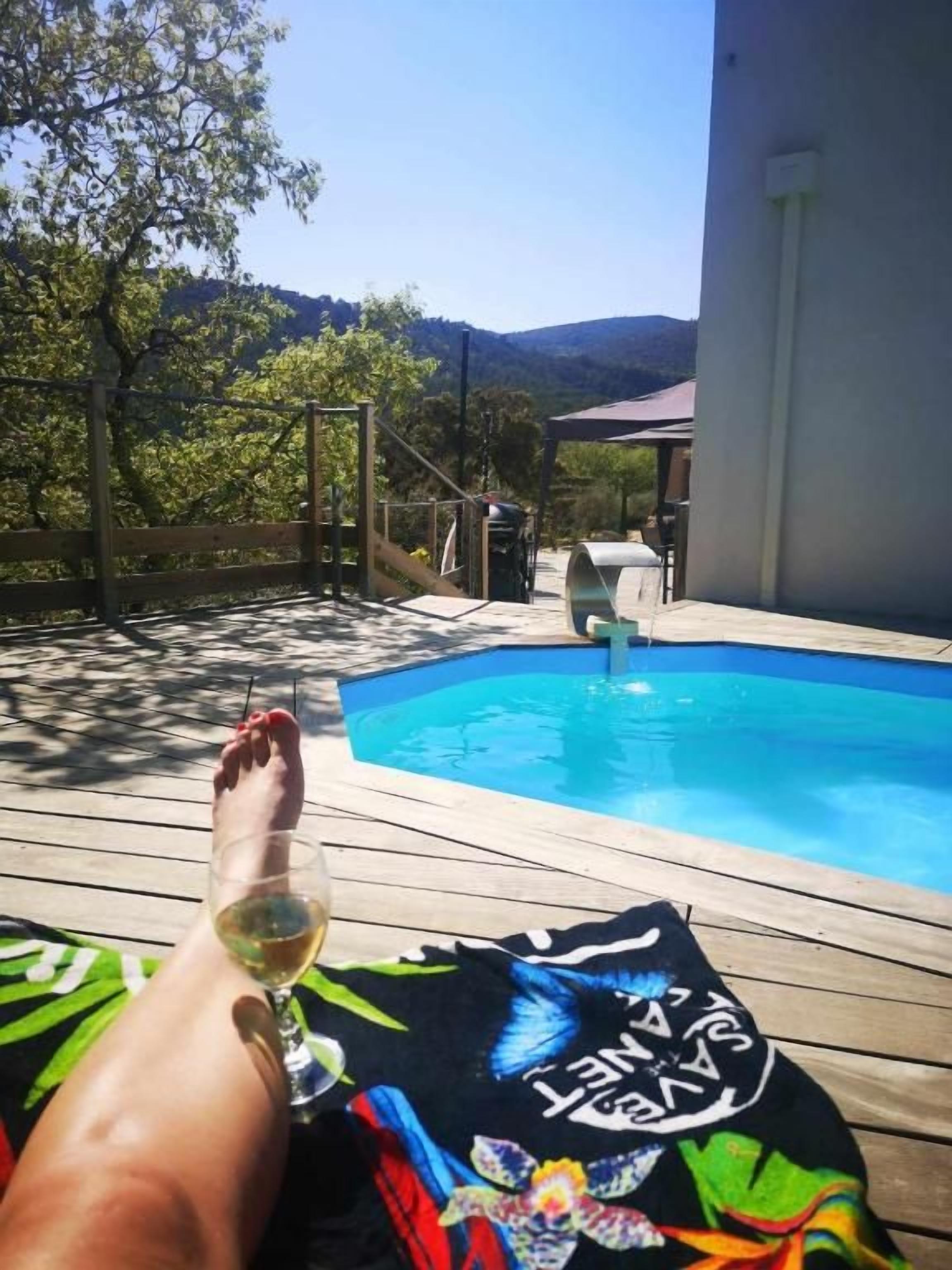 A poolside area with a wooden deck, a lounge chair, and a glass of wine.