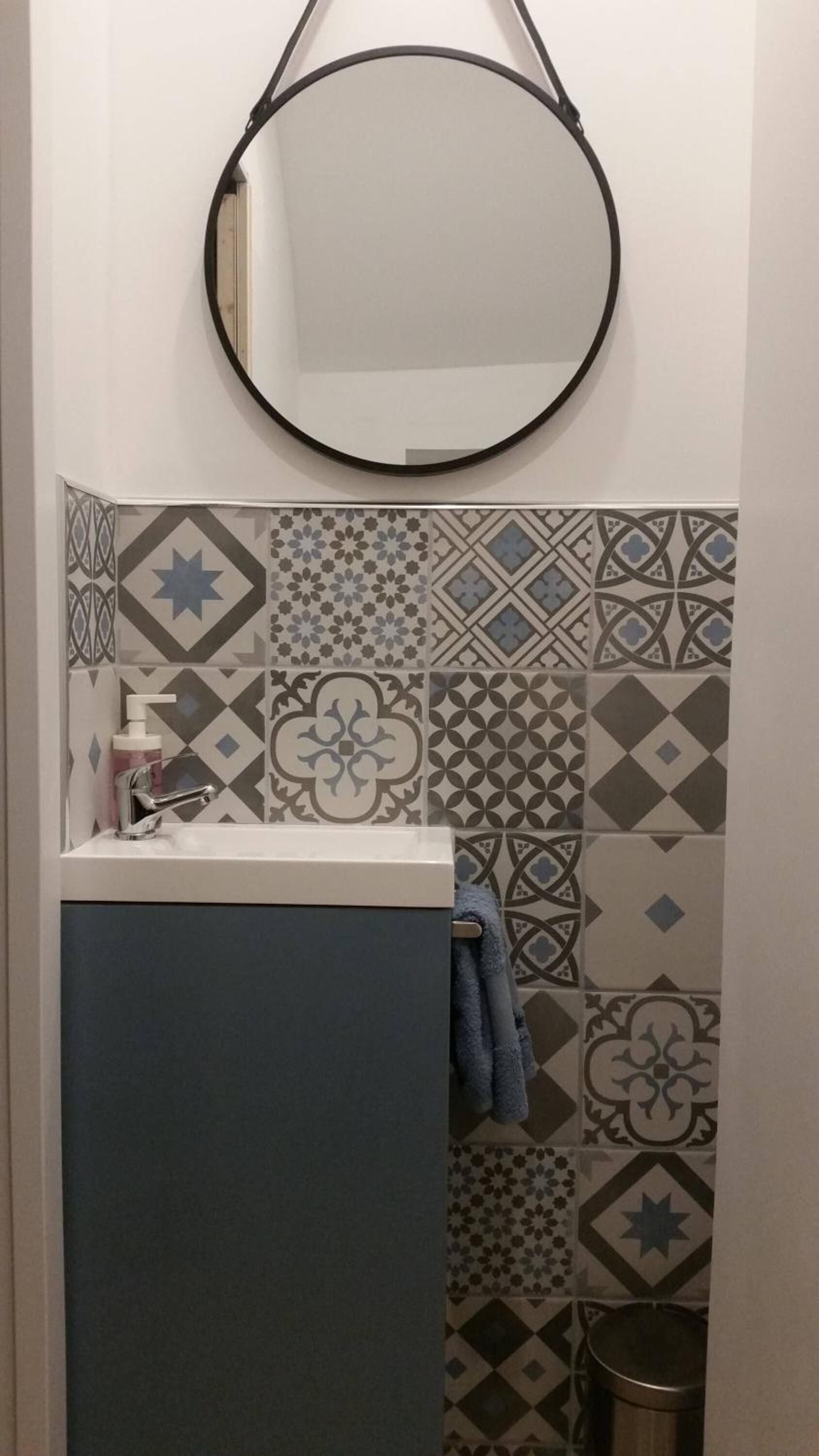A bathroom with a sink, a mirror, and patterned tiles.