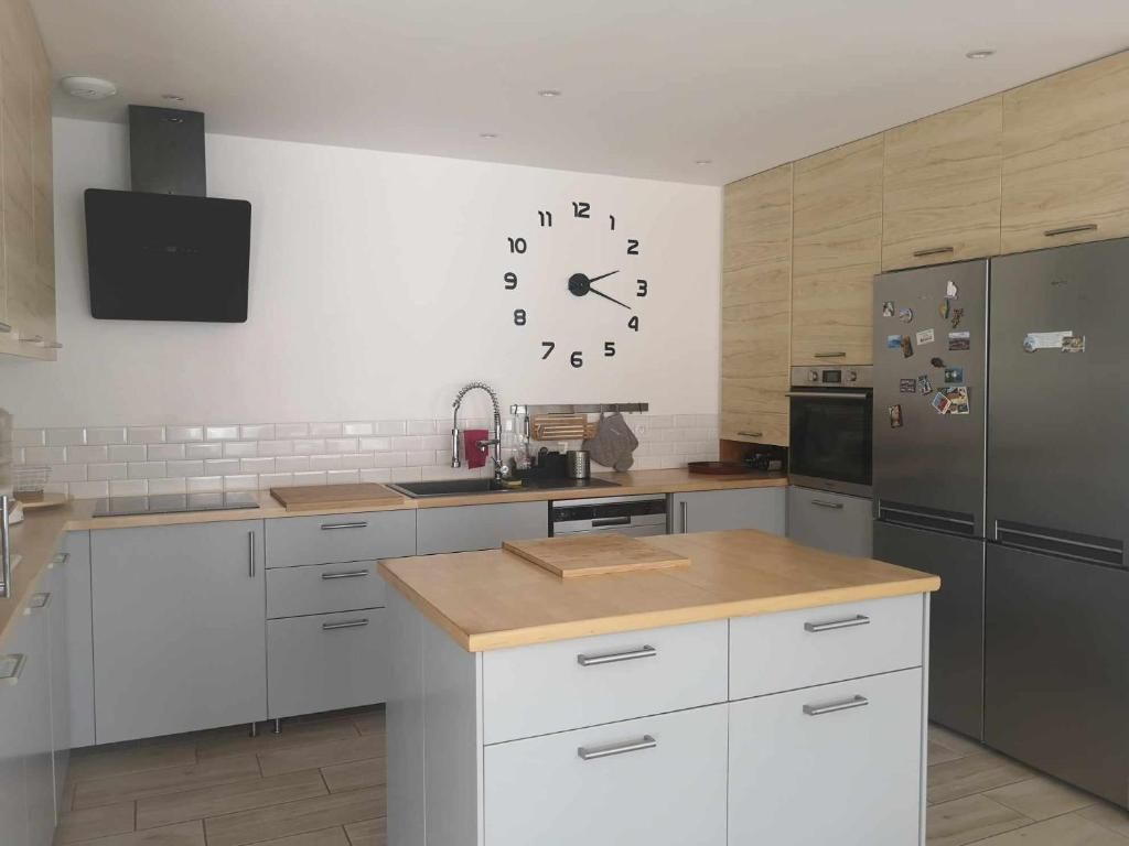 Una cocina moderna con una isla central, un reloj en la pared y electrodomésticos de acero inoxidable.