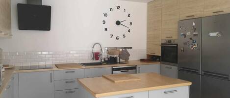 Una cocina moderna con una isla central, un reloj en la pared y electrodomésticos de acero inoxidable.