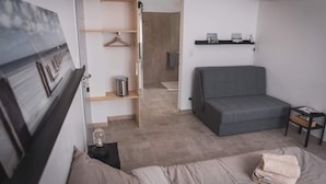A modern, compact living space with a grey sofa, a wooden shelving unit, and a small table with a towel. - Les chambres de Toucas (Sollies-Toucas)