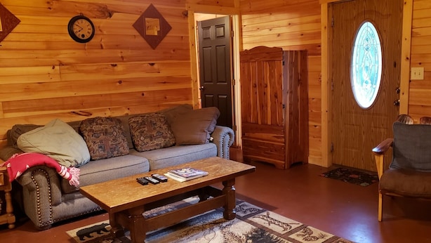 Un interior de cabaña acogedor con un sofá de madera, una mesa de centro, una silla y una puerta con un vitral.