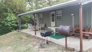 Un porche cubierto con mobiliario exterior, una parrilla y un ahumador.