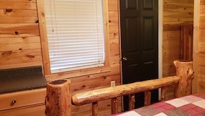 Interior de una cabaña con un banco de madera, una ventana con persianas, una puerta y una chimenea.