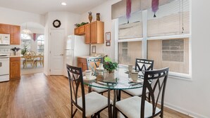 A modern kitchen with wooden cabinets, a glass dining table, and a view of the outside through large windows. - Villa Dodes by VillaDirect (Clermont)