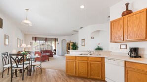 A spacious kitchen with wooden cabinets, a dishwasher, and a dining area with a table and chairs. - Villa Dodes by VillaDirect (Clermont)
