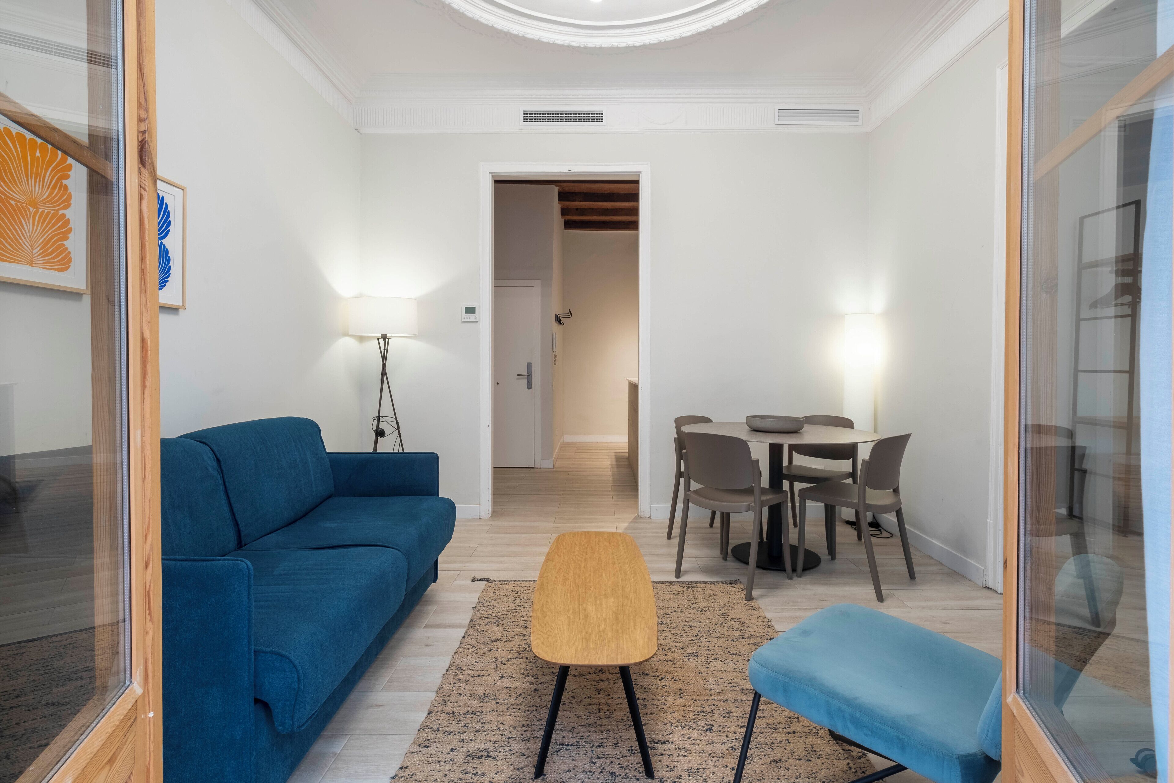 A modern living room with a blue sofa, a wooden coffee table, and a dining area with a table and chairs.