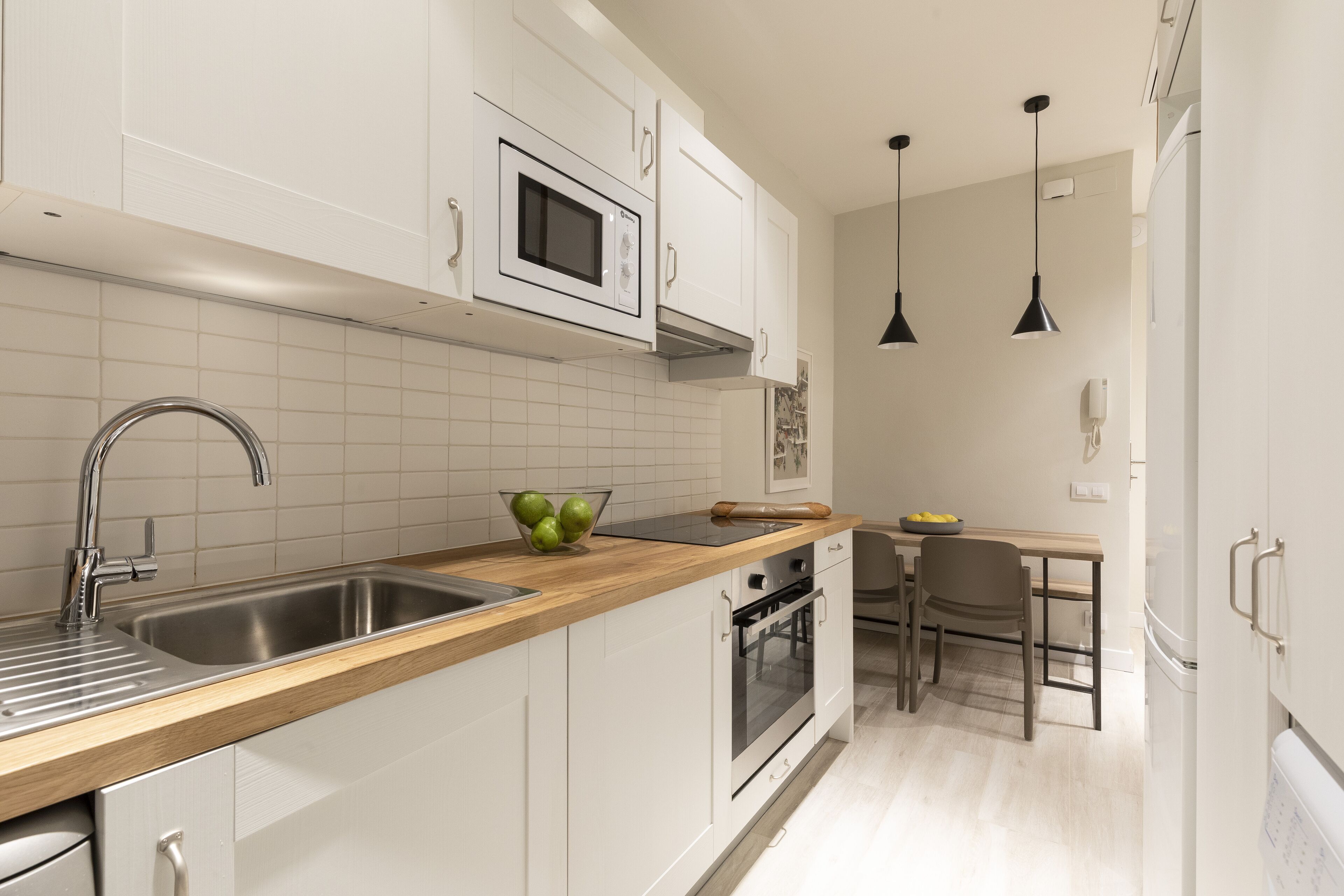 A modern kitchen with white cabinets, stainless steel appliances, a wooden countertop, and a built-in oven.
