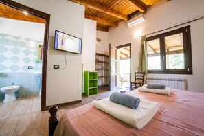 A bedroom with a wooden ceiling, a bed with towels, a television, and a view of the outside through a window. - Sa Tanchitta (Ula Tirso)
