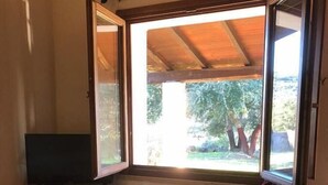 Une pièce avec un sol carrelé, une table recouverte d’une nappe à motifs, un téléviseur posé sur la table et une fenêtre avec un rideau.