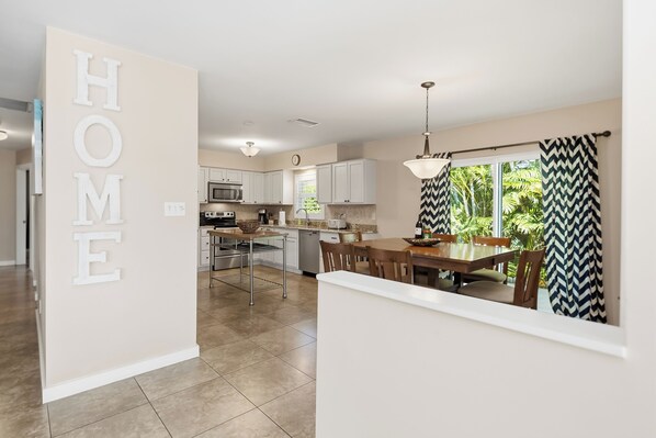 A modern kitchen with white cabinets, a stainless steel refrigerator, and a dining area with a table and chairs. - Top‘s Naples Park Home, sleeps 6 adults + toddlers, close to beach, near all! (Naples)