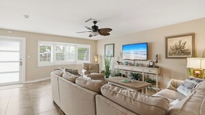 A spacious living room with a beige sofa, a coffee table, and a television on the wall. - Top‘s Naples Park Home, sleeps 6 adults + toddlers, close to beach, near all! (Naples)